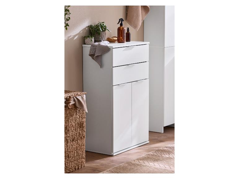 Witte badkamerkast met lades en deuren, planten en bruine flessen erbovenop.