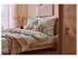 Slaapkamer met groen beddengoed met patroon, een beige plaid en een houten bedframe.
