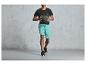 Man in zwarte sportshirt en blauwe shorts met een trainingsbal.