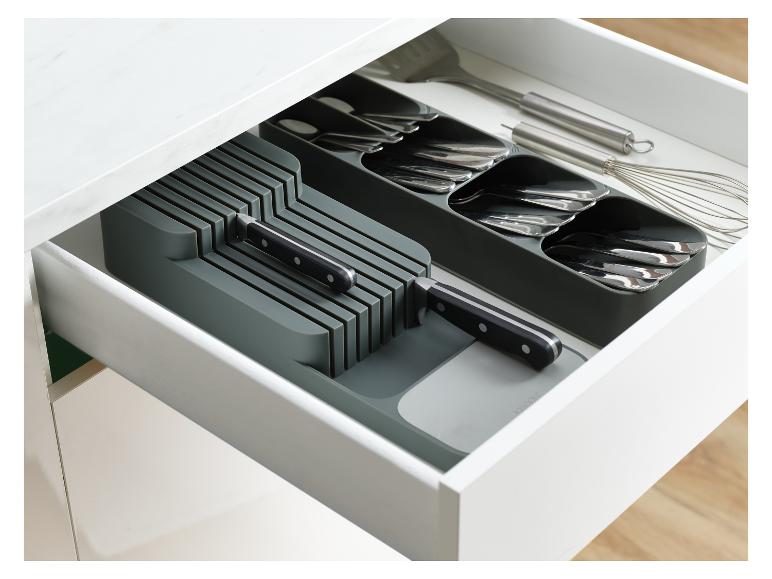 Een open keukenlade met een grijze bestekbak en messenblok, met diverse keukenhulpmiddelen.