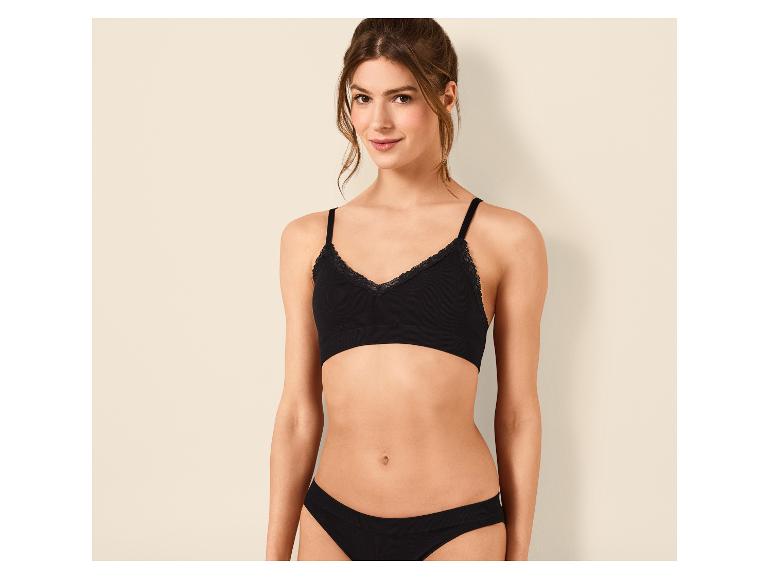 Vrouw in zwarte beha en slip met kant, poserend voor een muur.