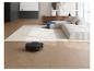 Robotstofzuiger reinigt houten vloer in moderne woonkamer met bank en vloerkleed.