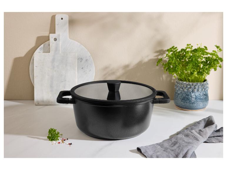 Zwarte kookpan met glazen deksel, marmeren snijplanken en verse peterselie.