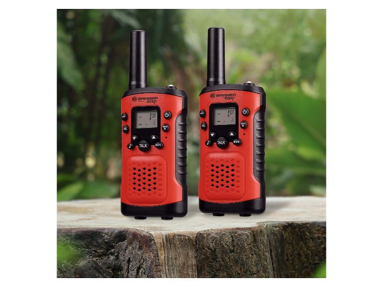 Twee rode en zwarte walkietalkies op een houten ondergrond met een groene, wazige achtergrond