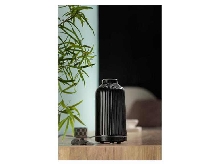 Een zwarte keramische etherische oliën diffuser op een houten oppervlak naast een plant.