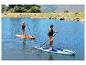 Twee mensen peddelen op CRIVIT Allround SUP boards op een meer, omringd door heuvels en bomen.