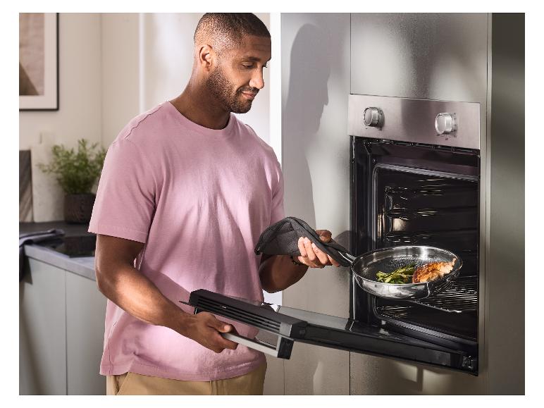 Een man gebruikt een pannenlap om een roestvrijstalen pan met eten in de oven te schuiven.