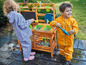 Twee kinderen spelen met water in een houten speelkeuken.