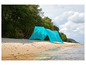 Een blauwe tent op een zandstrand met bomen op de achtergrond.