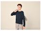 Jongen in donkerblauw shirt met lange mouwen en lichte jeans, met grijze hoodie over zijn schouder.