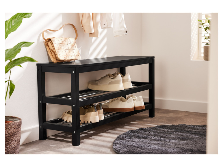 Een zwarte schoenenrek met witte sneakers en een rieten tas.