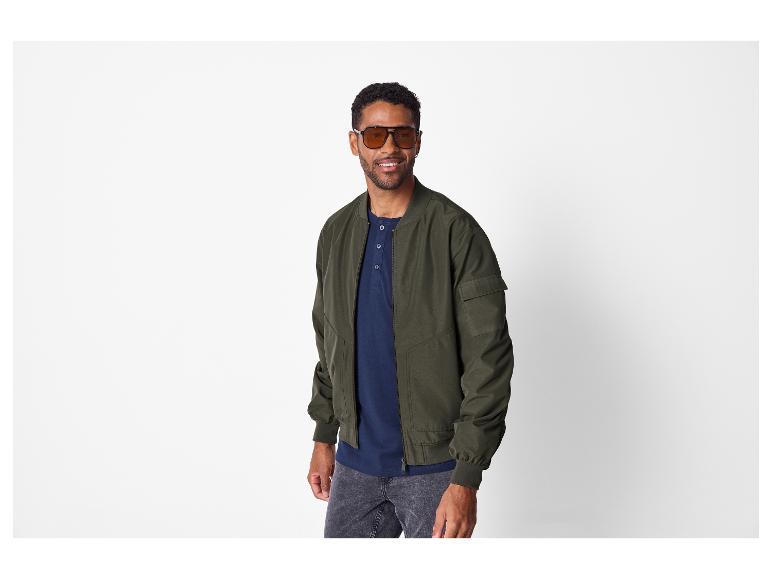 Man in een donkergroen bomberjack, marineblauw henley-shirt en donkere jeans