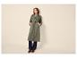 Vrouw in groene trenchcoat, jeans en bruine loafers.