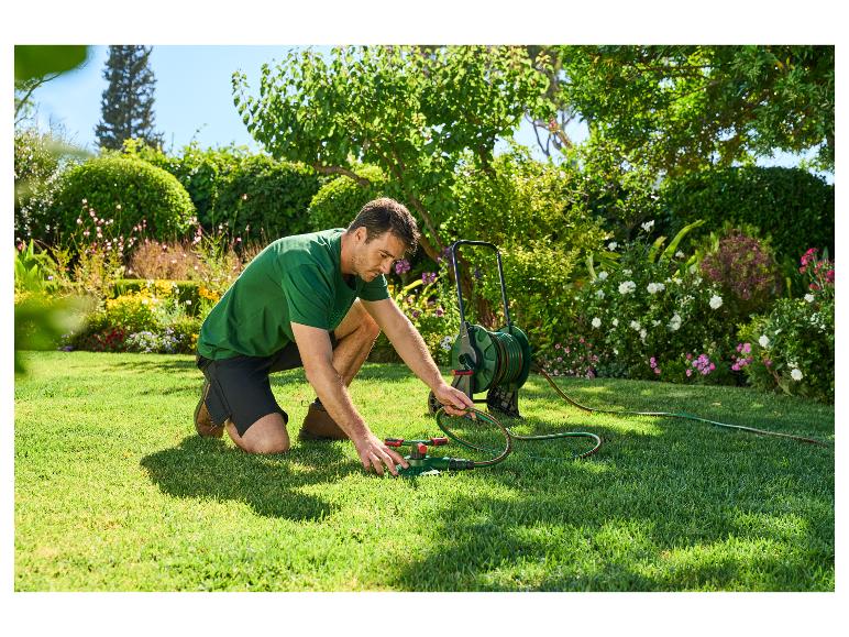 Man sluit een sproeier aan op een tuinslang op een gazon.