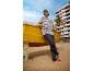 Man in gestreept T-shirt en donkere broek leunend op een gele boot op het strand.