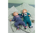 Twee baby's in blauwe en groene babykleding op een groene bladerenmat.