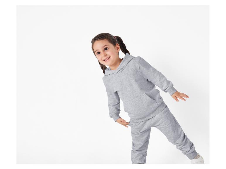 Een jong meisje draagt een grijze hoodie en joggingbroek.