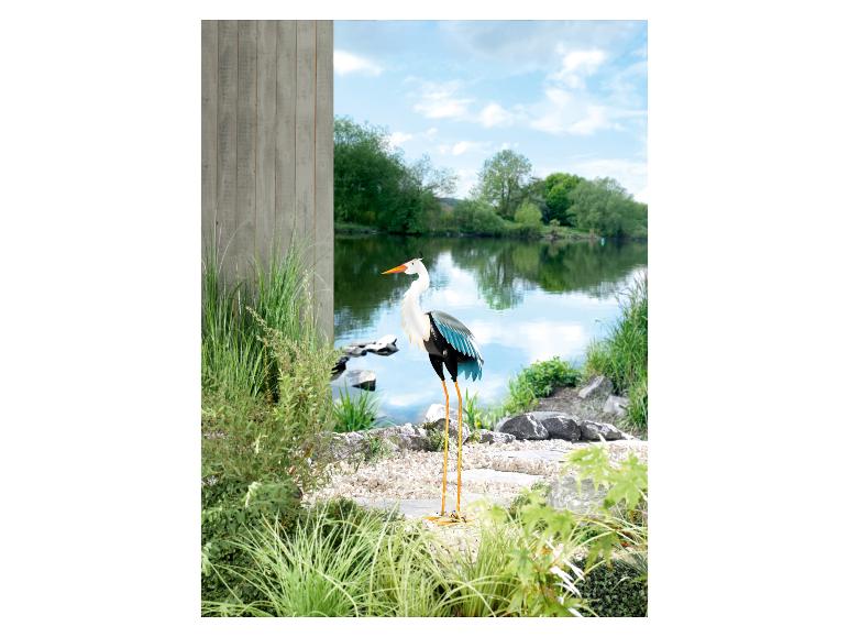 Een metalen reiger decoratie in een tuin met een vijver.