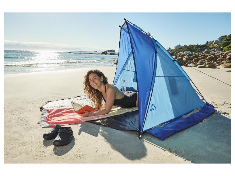 Vrouw leest boek in strandtent op zandstrand met zee op de achtergrond.
