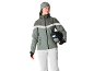 Vrouw met grijze muts, groene ski-jas en witte broek, houdt een helm vast.