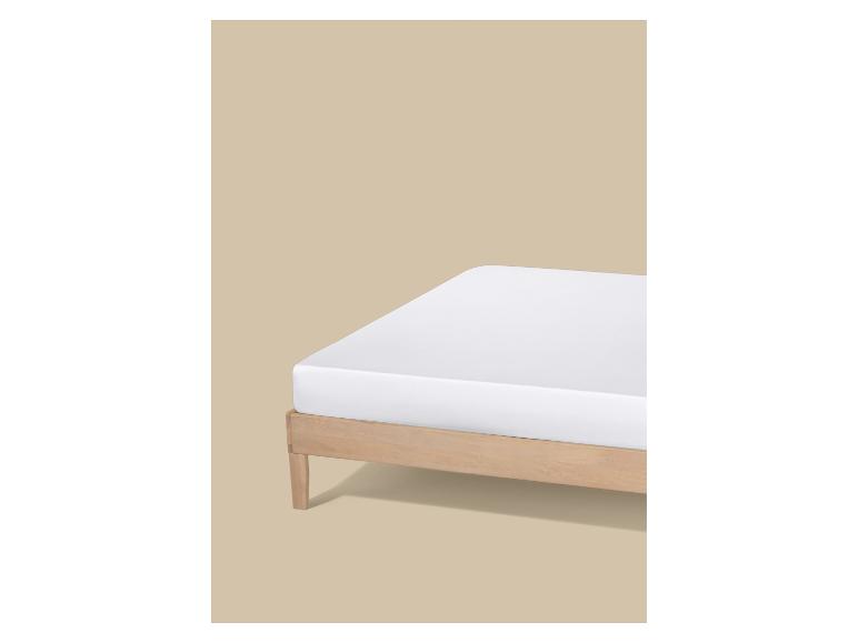 Wit matras op een licht houten bedframe tegen een beige achtergrond.