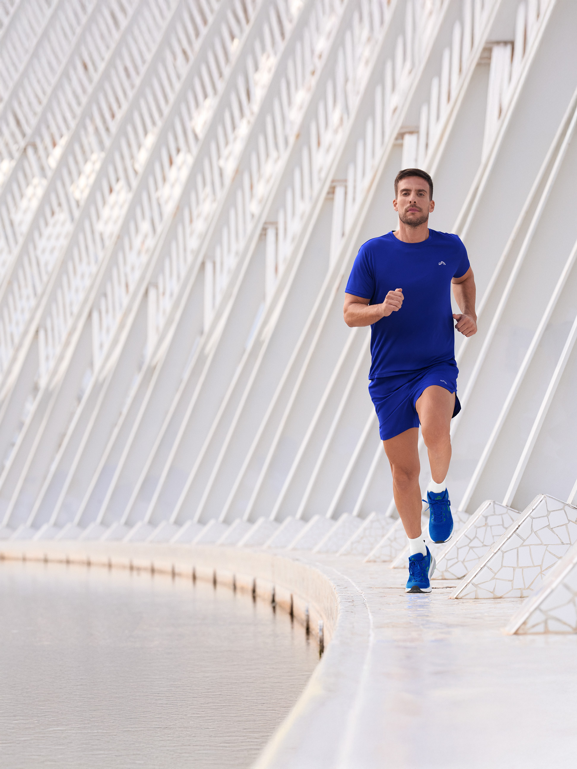 Man in blauwe sportkleding, rennend langs een waterpartij.