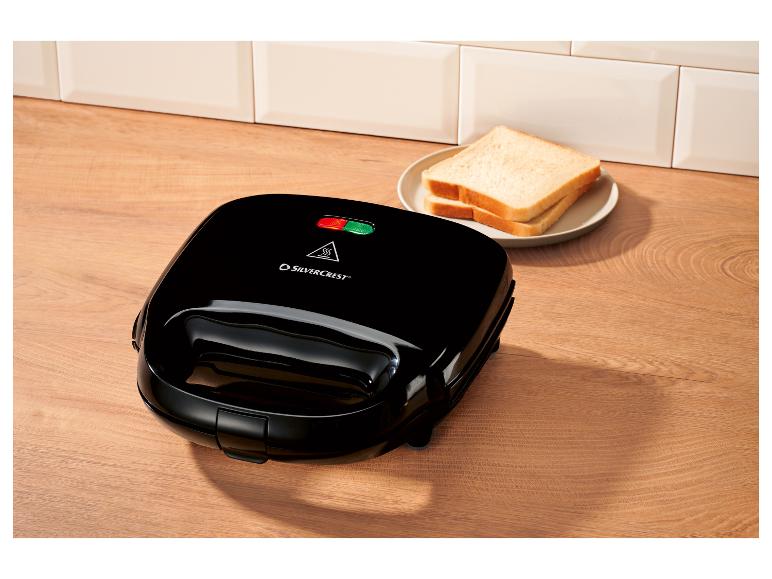 Zwart tosti-apparaat met twee sneetjes brood op een bord op een houten ondergrond.