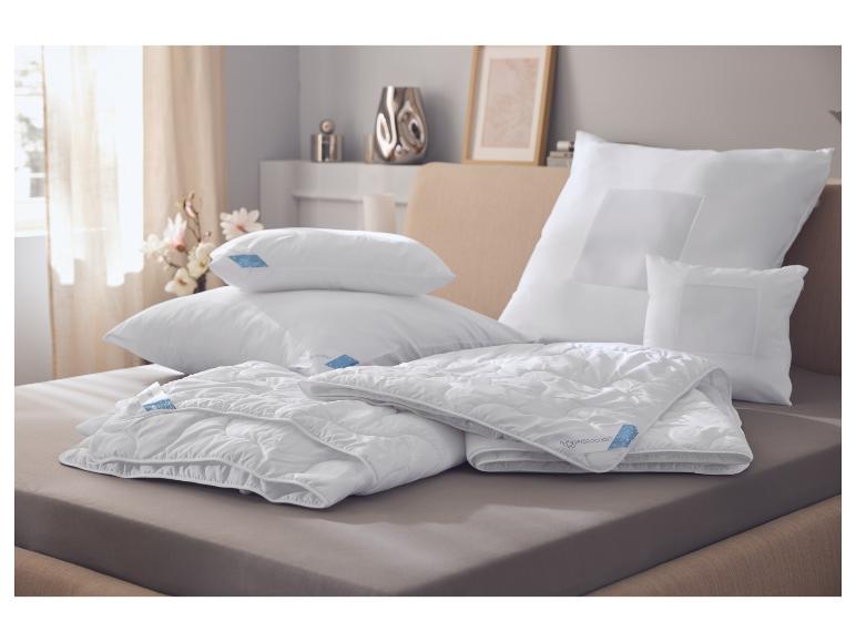 Witte kussens en dekbedden met blauwe Hydrocool labels op een bed in een slaapkamer.