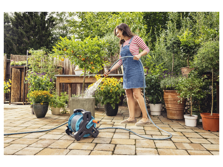 Een vrouw gebuikt een Gardena tuinslang om planten in potten water te geven.