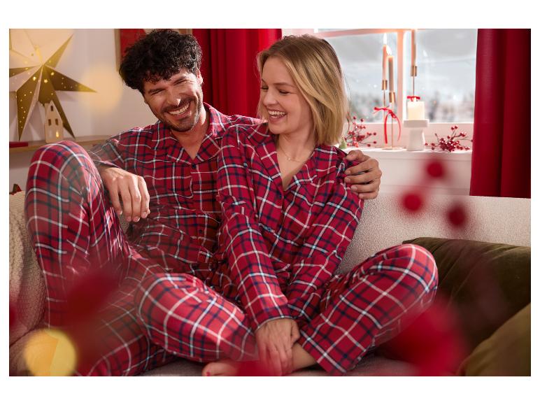 Gelukkig stel in rode geruite pyjama, ontspannend op een kerstbank.