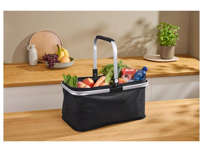 Zwarte boodschappenmand met boodschappen, waaronder fruit, groenten en water, op een aanrecht.