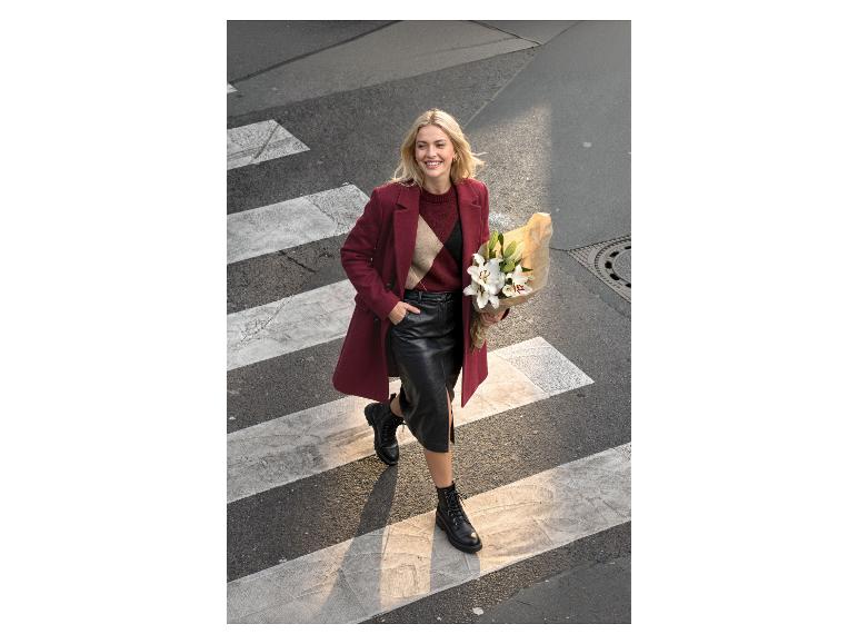 Vrouw in rode jas, zwarte leren rok en laarzen steekt zebrapad over met bloemen.