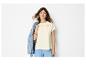 Vrouw in geborduurd T-shirt, blauwe broek en spijkerjack over schouder.