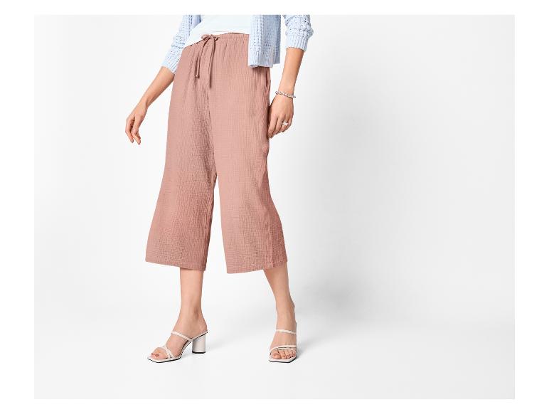 Vrouw draagt roze culottes, een witte top en een lichtblauw vest, met witte sandalen met hak.