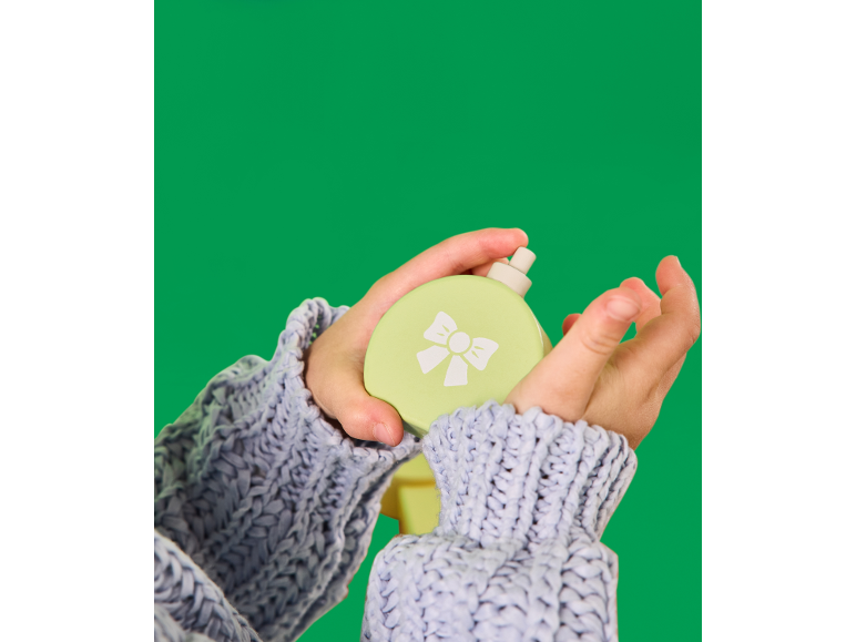 Handen houden een lichtgroene spuitfles met een witte strik vast, tegen een groene achtergrond.