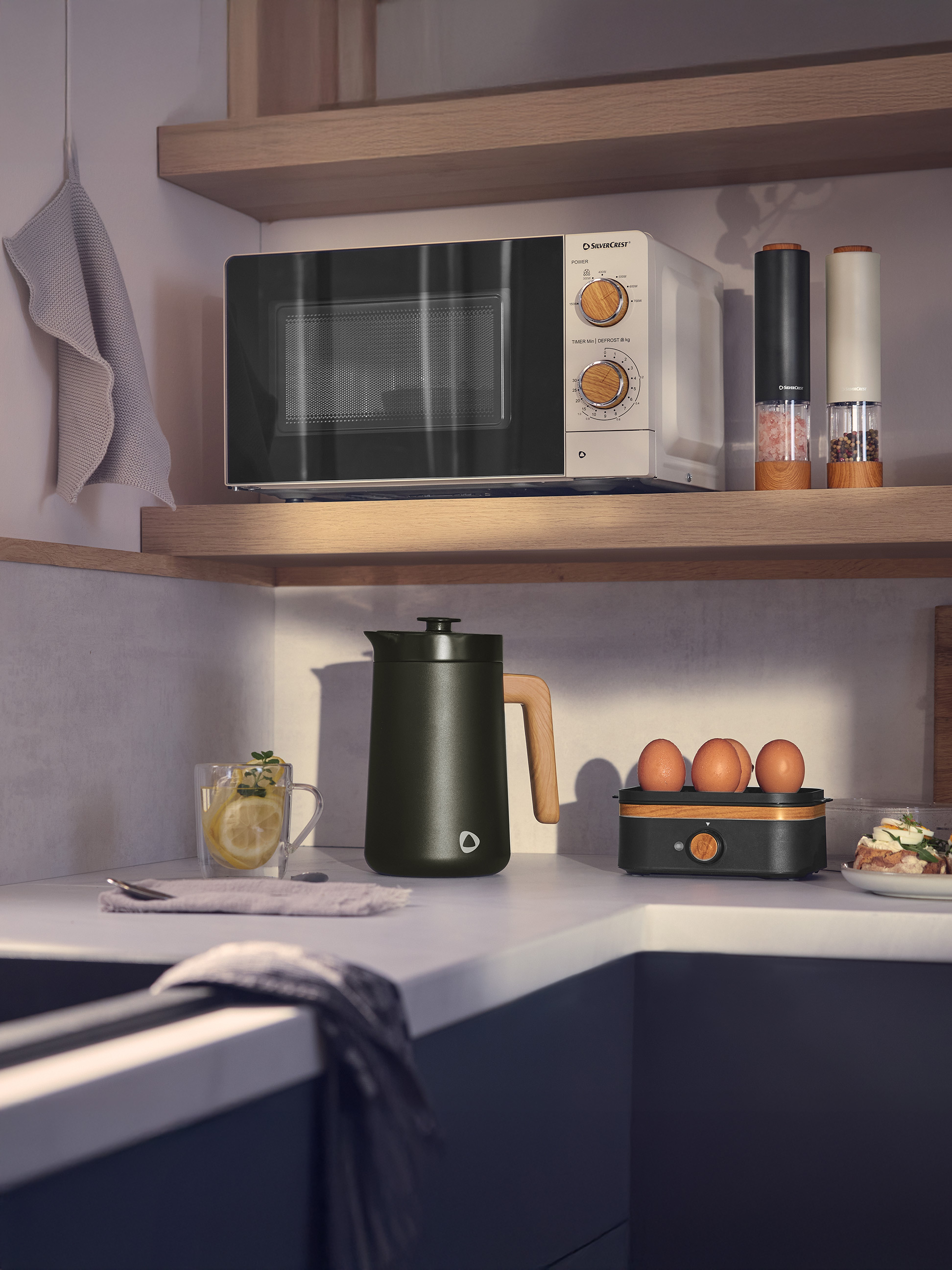 Witte en zwarte magnetron met houten details, donkergroene waterkoker en keukengerei in een moderne keuken.