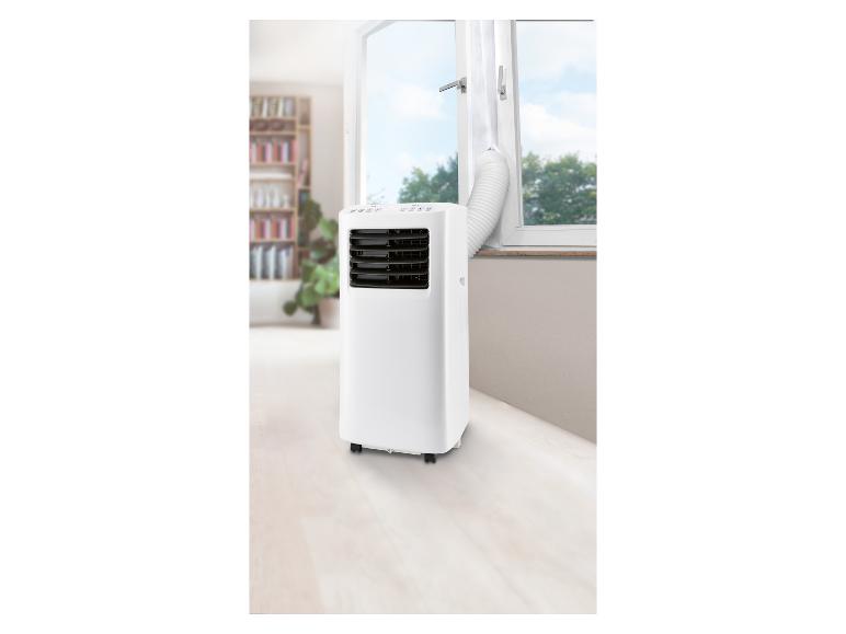 Witte mobiele airconditioner met afvoerslang die door een open raam naar buiten leidt.