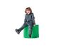 Lachend kind in een grijs hooded trainingspak en zwarte schoenen, zittend op een groene cilinder.