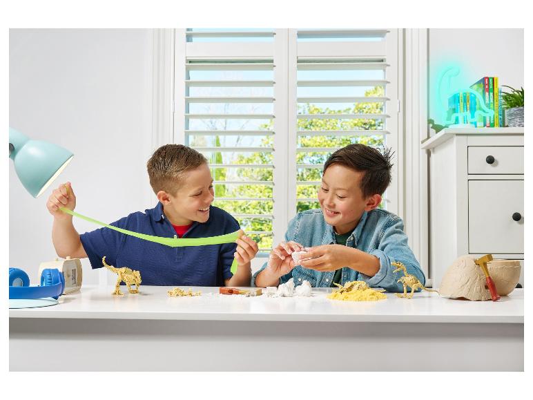 Twee jongens spelen met dinosaurusspeelgoed en slijm aan een tafel.