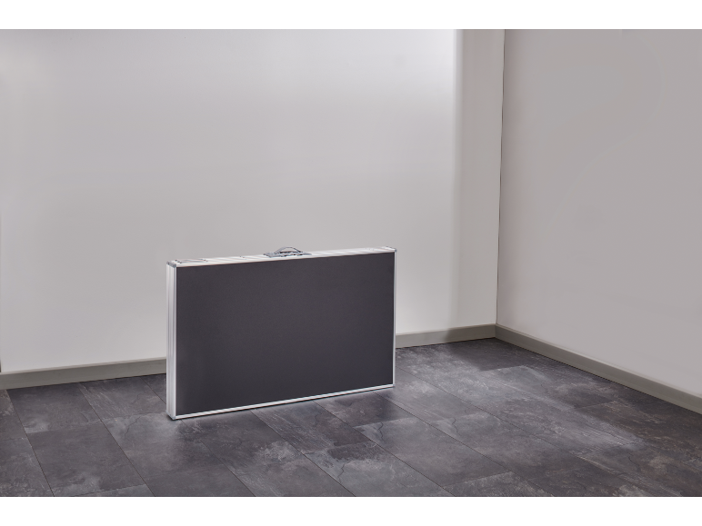 Een donkergrijze opklapbare tafel in een koffer staat in een hoek van een kamer met een grijze vloer.