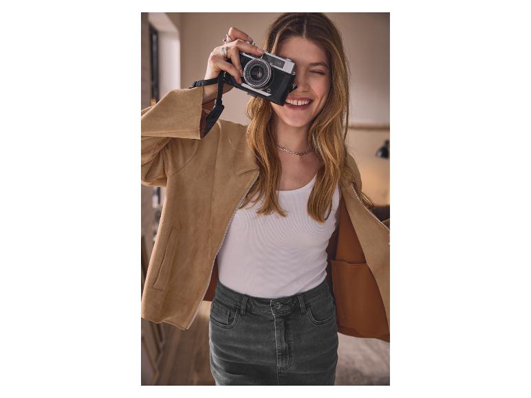 Vrouw in beige jas en jeansrok, die een foto maakt met een oude camera.