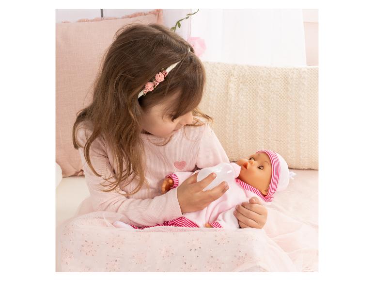 Meisje voedt een pop met een zuigfles, gekleed in roze.