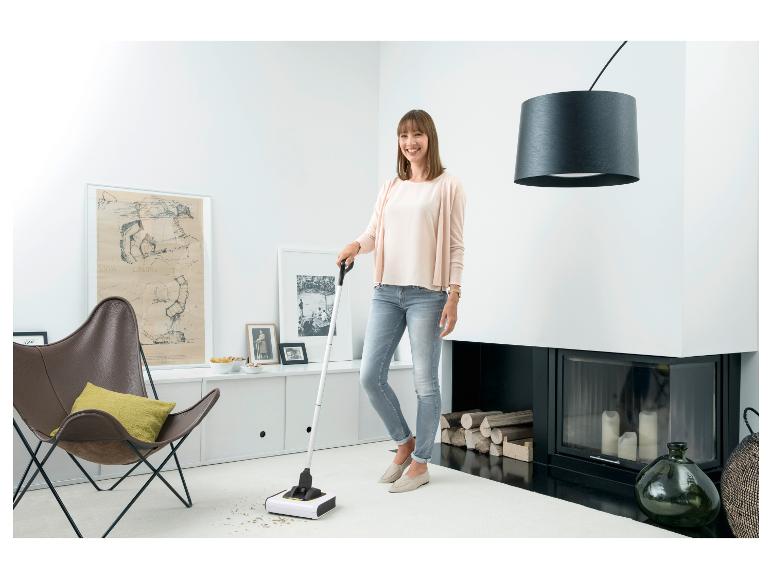 Vrouw maakt een witte woonkamer schoon met een veger en blik.
