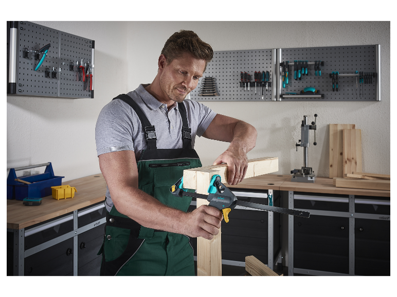 Een man gebruikt een Wolfcraft klem om houten onderdelen in zijn werkplaats te verbinden.
