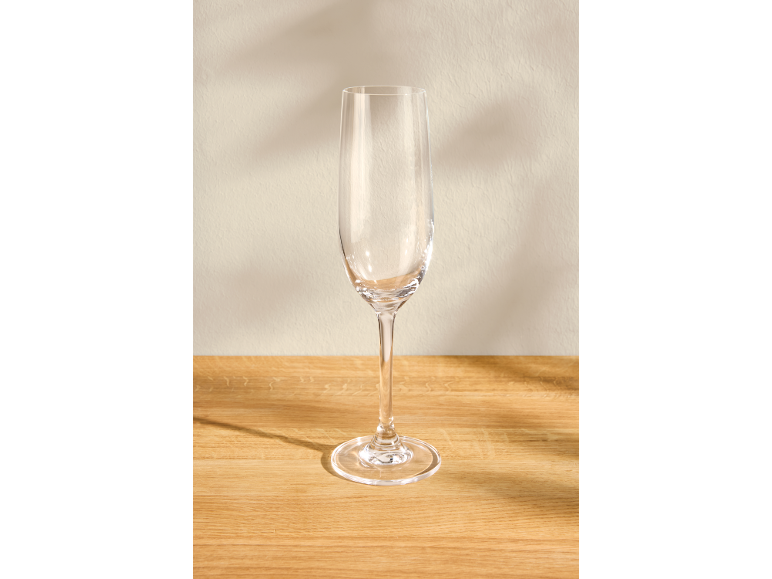 Leeg glazen champagneglas op een houten tafel met een lichte muur op de achtergrond.