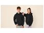 Twee tieners in zwarte hoodies en jeans, poserend tegen een beige achtergrond.