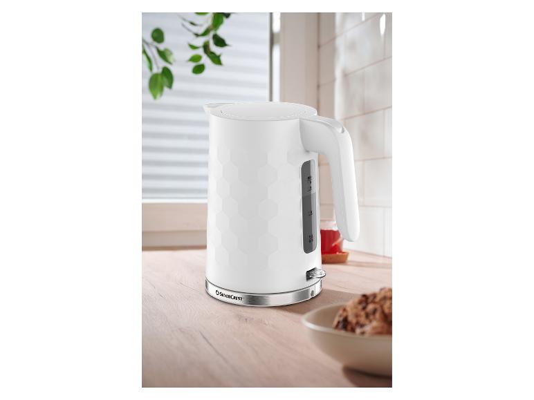 Witte waterkoker met honingraatpatroon op een houten aanrecht, naast een kom met koekjes.