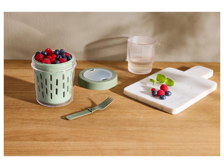 Snackcontainer met bosbessen, frambozen en rode bessen, naast een opvouwbare vork en een plank met fruit.