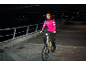 Vrouw in roze jas en zwarte broek op e-bike 's nachts