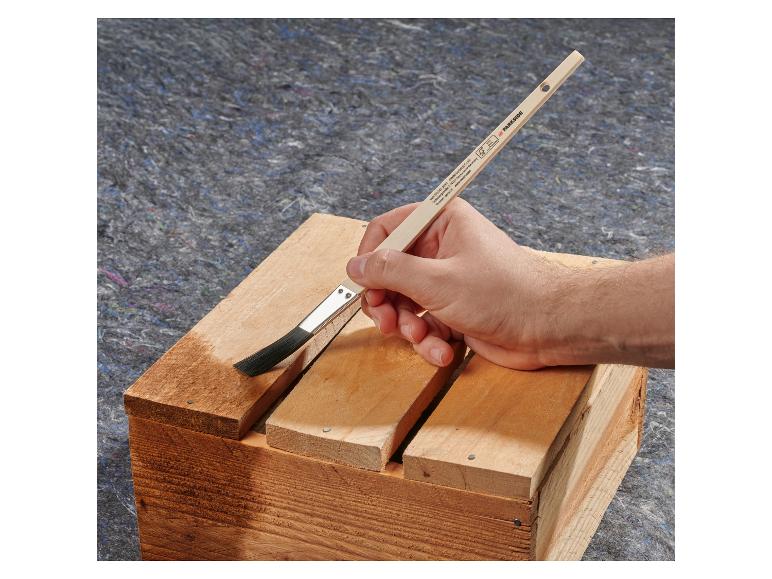 Hand brengt vernis aan op houten kist met kwast, op grijze achtergrond.